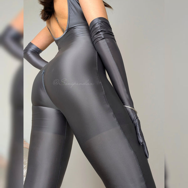 A woman posing in a dark gray glossy catsuit with matching gloves