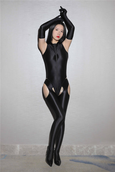 A woman in a black glossy bodysuit, matching elbow length gloves and suspender style pantyhose posing for a picture.