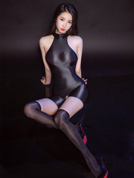 A woman posing in a black glossy unitard, featuring halter neck,an open crotch, and a black glossy sheer thigh high stockings.