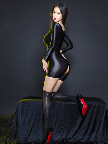 A woman posing in a black glossy unitard, featuring long sleeves, square neckline, an open crotch, and a black glossy sheer thigh high stockings.