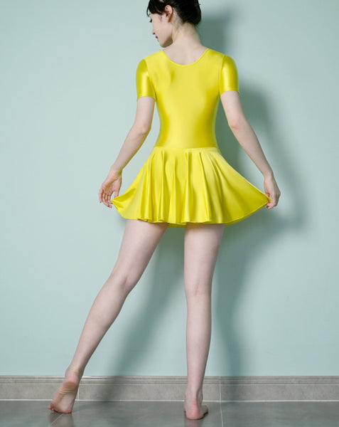 Back view of lady wearing yellow leotard dress featuring a scoop neckline, a scoop back cut, short sleeves, and an attached skirt.