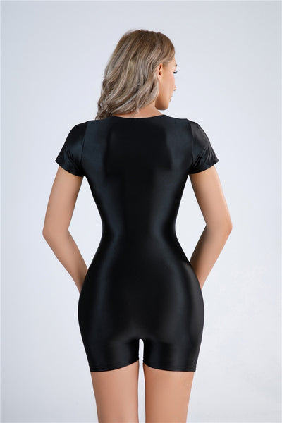 Back view of lady wearing a black color unitard featuring a scoop neckline, short sleeves, and a glossy stretchy fabric for all-day comfort.