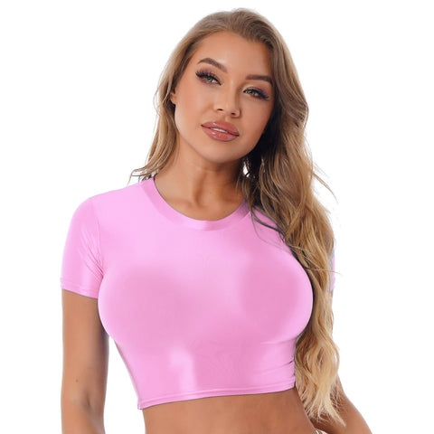 Front view of lady wearing pink crop top featuring a round neckline, short sleeves, and a stretchy and glossy fabric.