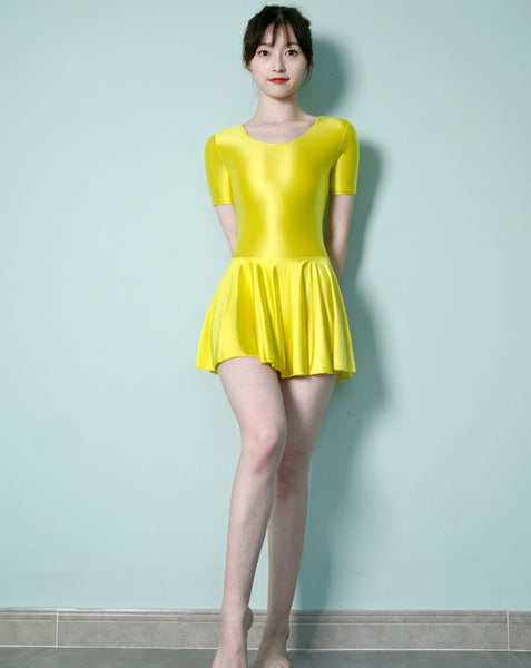 Front view of lady wearing yellow leotard dress featuring a scoop neckline, a scoop back cut, short sleeves, and an attached skirt.